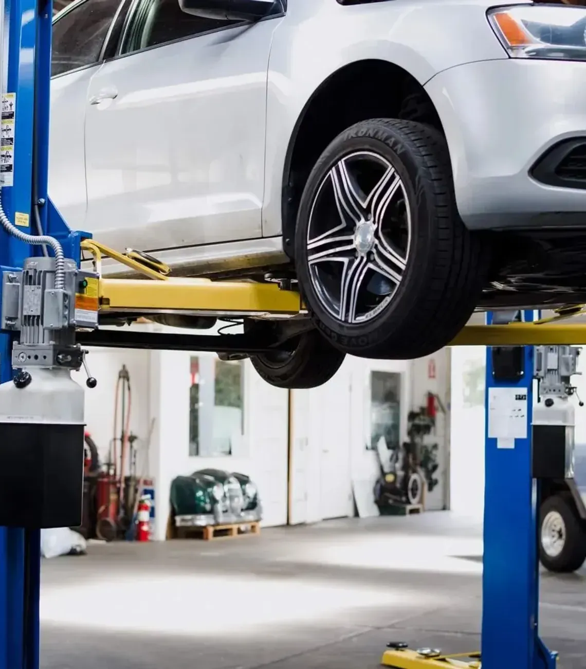 A silver sedan raised on a two-post automotive lift inside a repair shop.