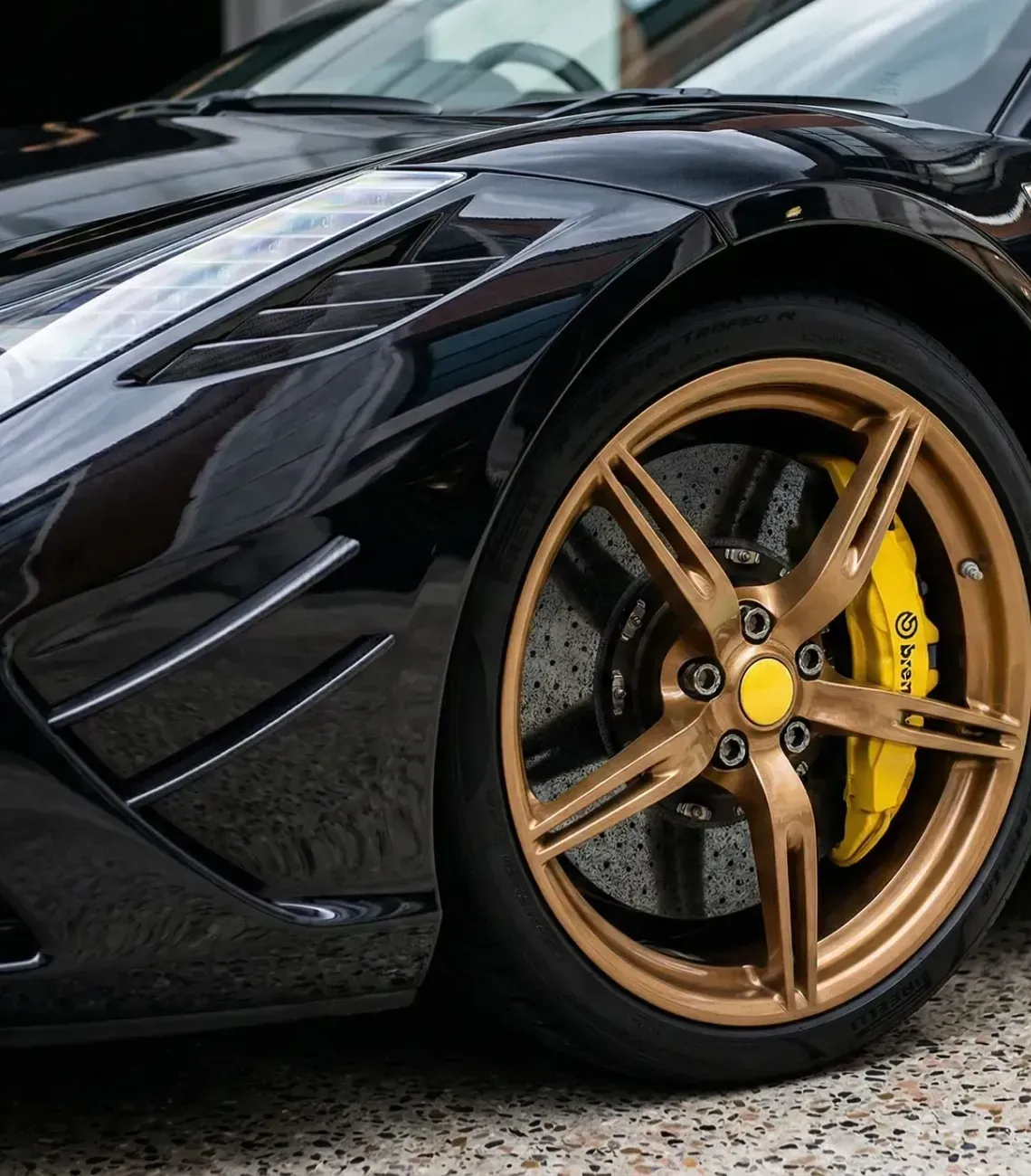 Close-up of a black sports car's front fender and wheel with gold rims and a yellow brake caliper.