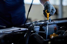 A mechanic wearing gloves checks a car engine's oil level using a dipstick.