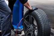 A mechanic wearing black gloves holds a car tire and wheel assembly in a repair shop.