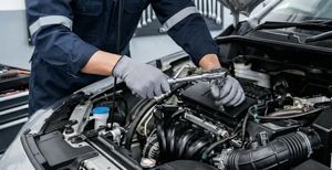 A mechanic wearing gloves uses a ratchet tool to work on a car engine in an auto repair shop.
