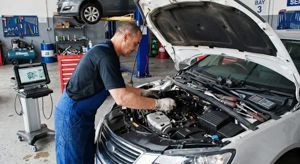 A technician in blue coveralls works on an open car engine in a professional repair shop.