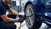 A mechanic wearing black gloves uses a pneumatic impact wrench to tighten a bolt on a car wheel in an auto repair shop.