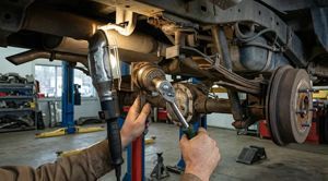 A mechanic uses a ratchet to work on the rear axle and suspension of a vehicle raised on a lift in an auto repair shop.
