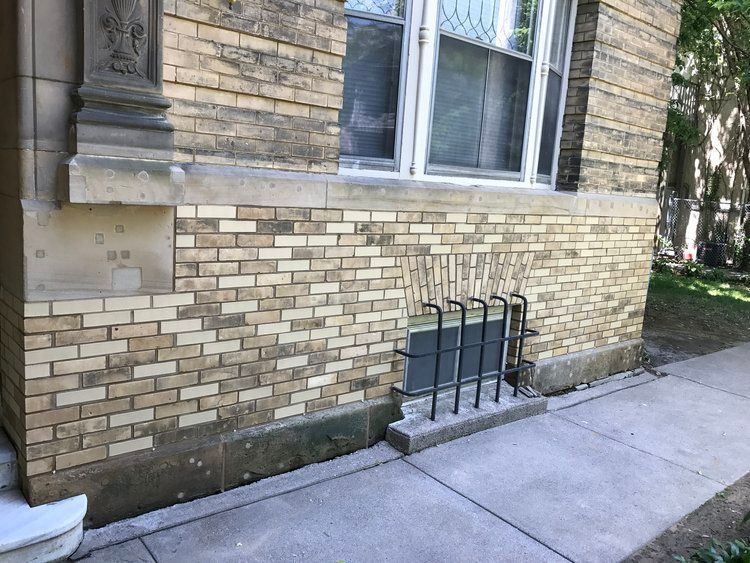 A brick building with a window and a sidewalk in front of it.