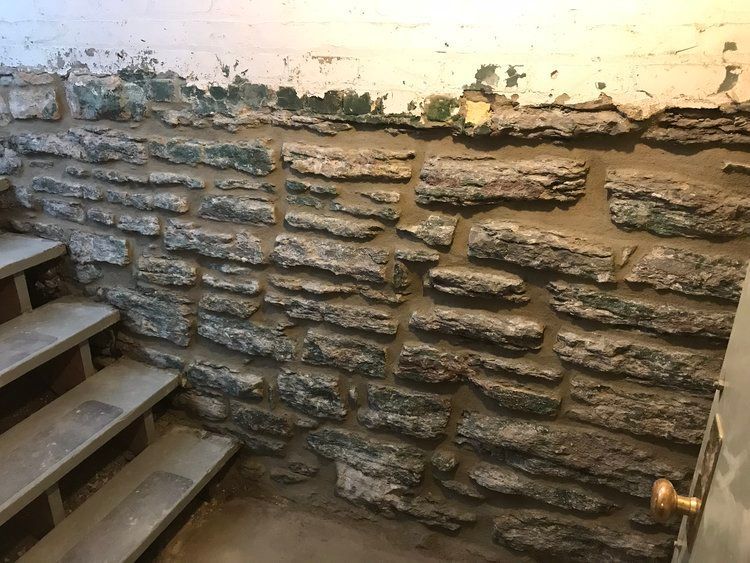 A stone wall with stairs leading up to it in a basement.