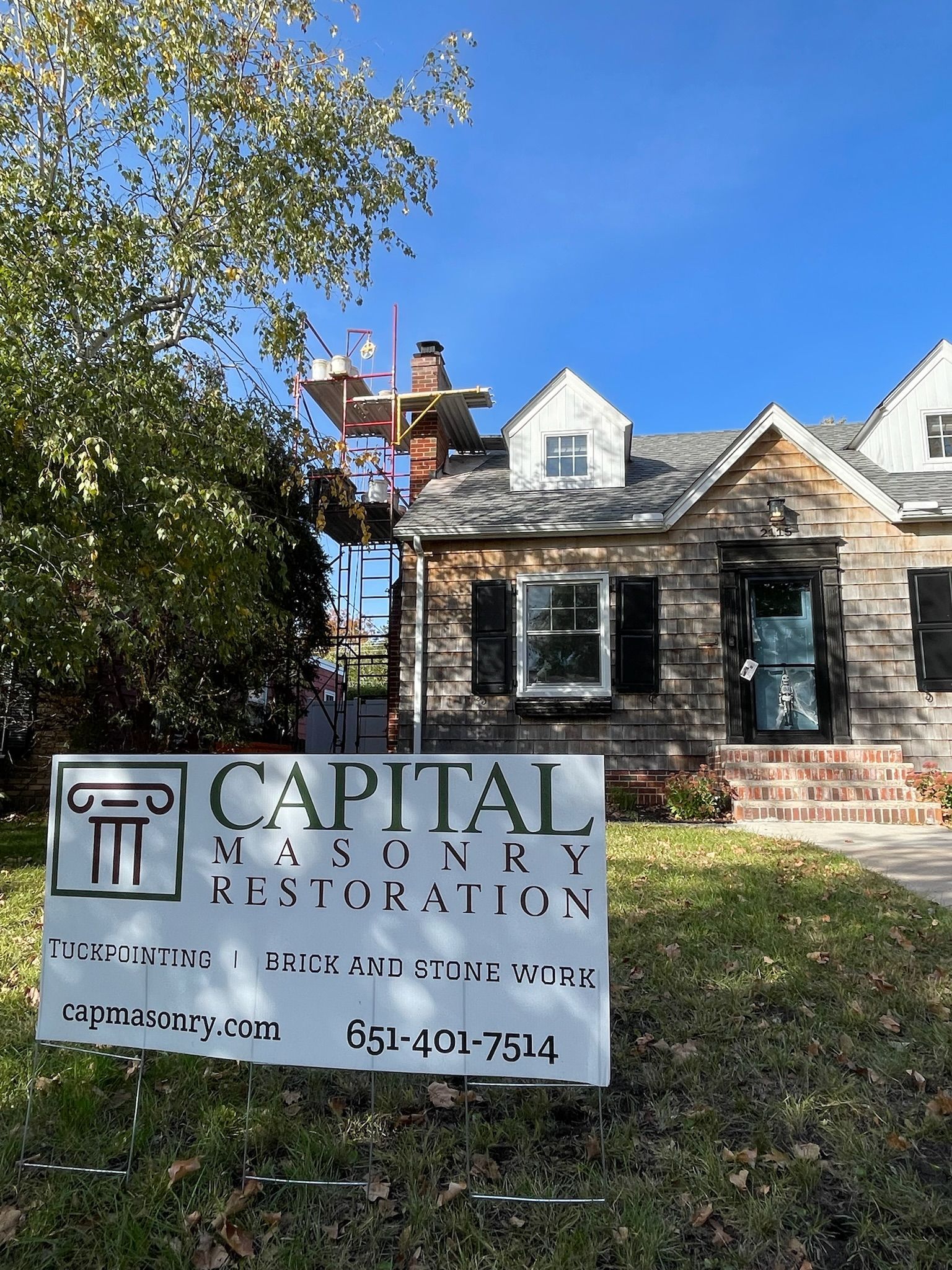 A man is working on a crane on the side of a brick building.