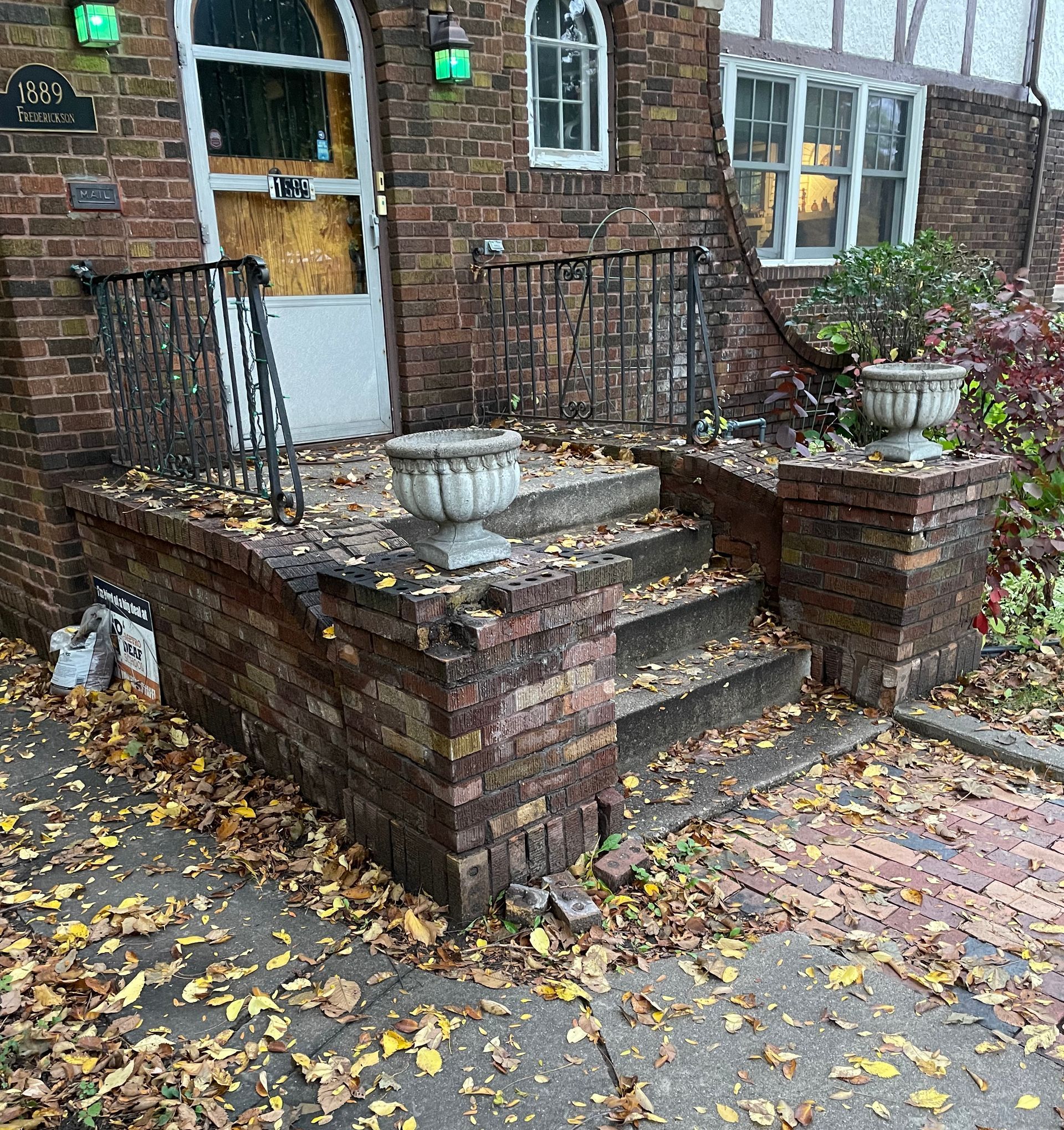 A brick house with a porch and stairs covered in leaves.