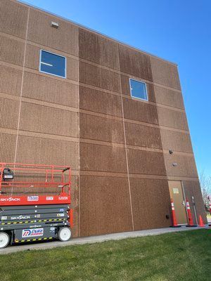 A red scissor lift is parked in front of a large brown building.