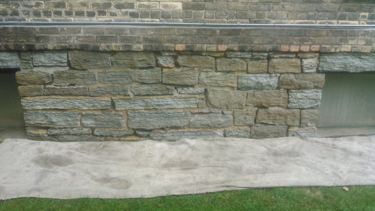 A stone wall next to a brick wall with a window in it.