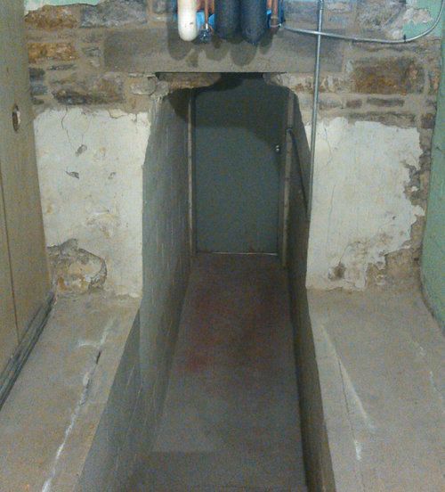 A narrow tunnel in a basement with pipes coming out of it.