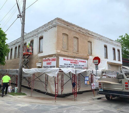 A large white building is being painted and covered in tarps.