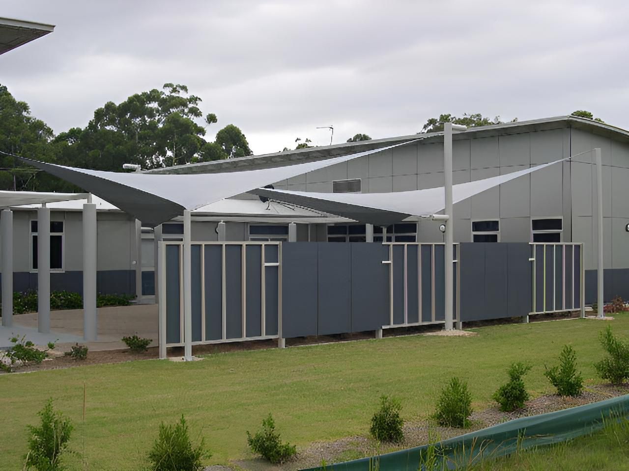 A Building with A Fence and Umbrellas in Front of It — Jon Wilson Canvas & Shade in Coffs Harbour, NSW