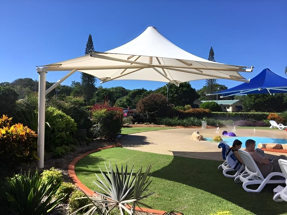 A Group of People Are Sitting Under an Umbrella Near a Pool — Jon Wilson Canvas & Shade in Coffs Harbour, NSW