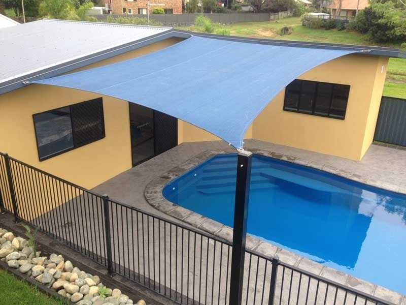 Blue Shade Sail Over a Swimming Pool Next to a Yellow House With Black Framed Windows