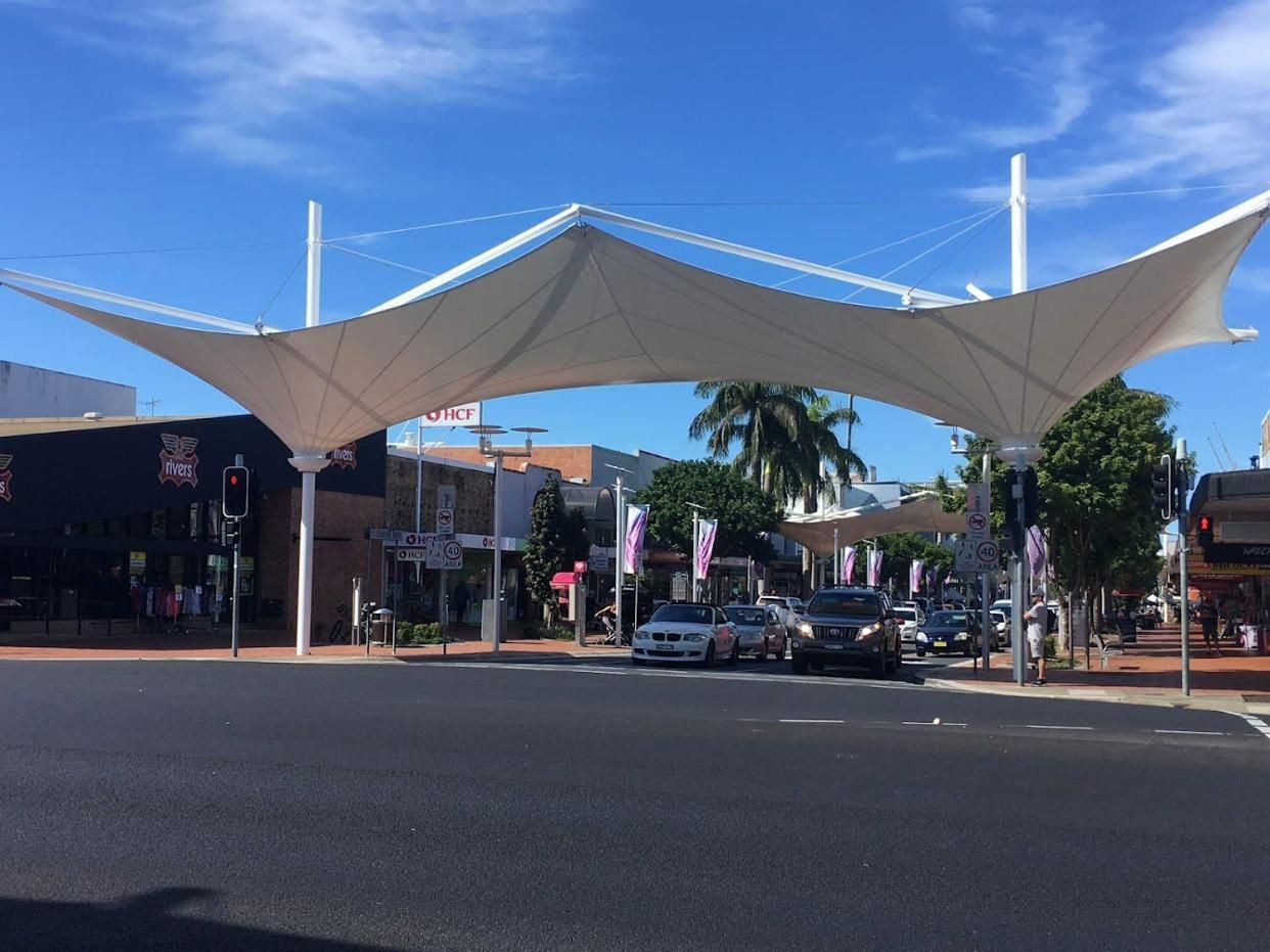A Large White Umbrella Is Over a Street with Cars Driving Underneath It — Jon Wilson Canvas & Shade in Coffs Harbour, NSW
