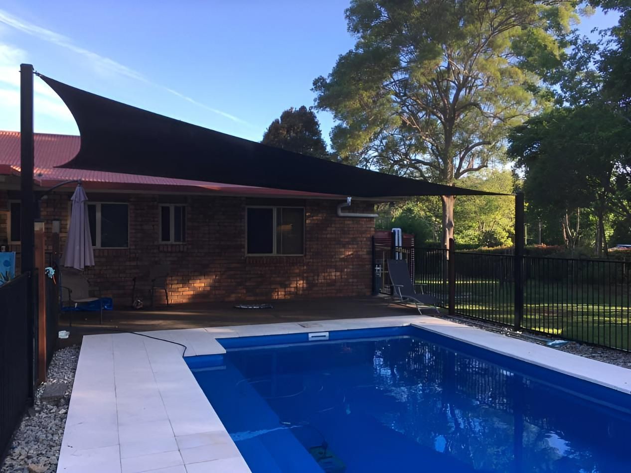A Large Swimming Pool Is Surrounded by A Fence and A Brick House — Jon Wilson Canvas & Shade in Coffs Harbour, NSW