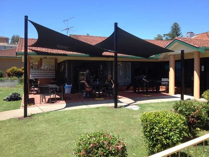 A Group of People Are Sitting Under a Shade Sail in Front of A House — Jon Wilson Canvas & Shade in Coffs Harbour, NSW