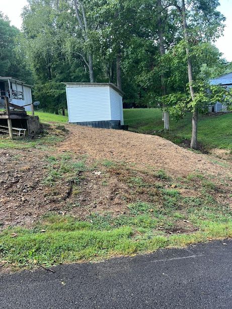 A small white house is sitting on top of a dirt hill next to a road.