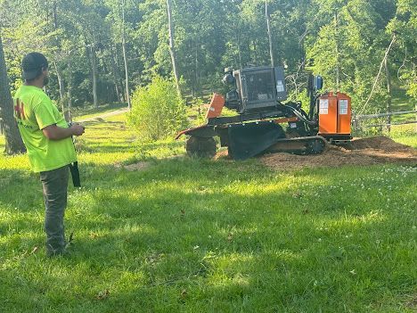 A man is standing in front of a stump grinder in a grassy field.