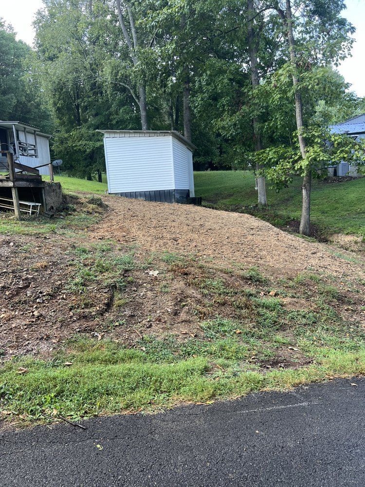 A white shed is sitting on top of a grassy hill next to a road.
