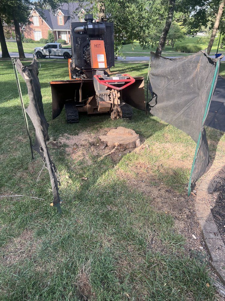 A stump grinder is sitting in the grass next to a fence.