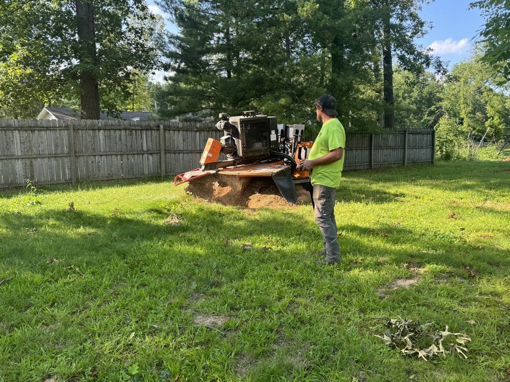 A man is standing in front of a stump grinder in a yard.
