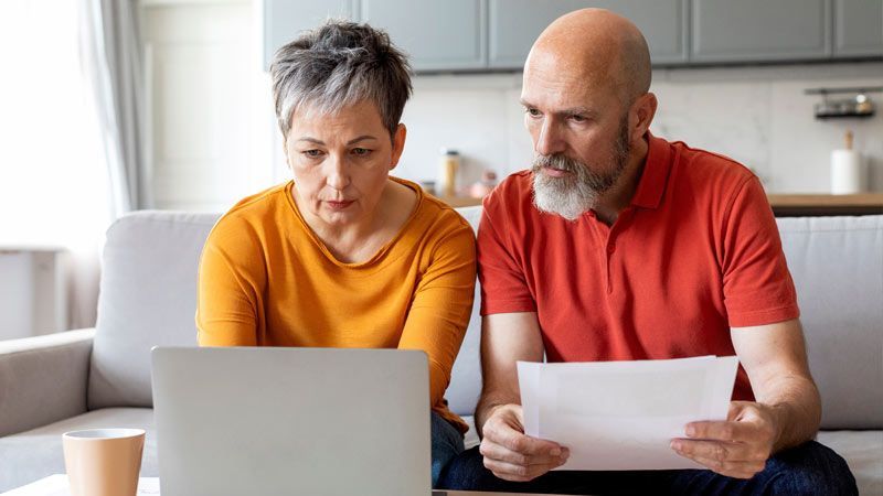 A couple sits on a couch, looking at a laptop together, reading college financial aid material