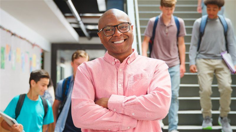 A man  standing in a hallway with his arms crossed. Top Questions to Ask College Recruiters