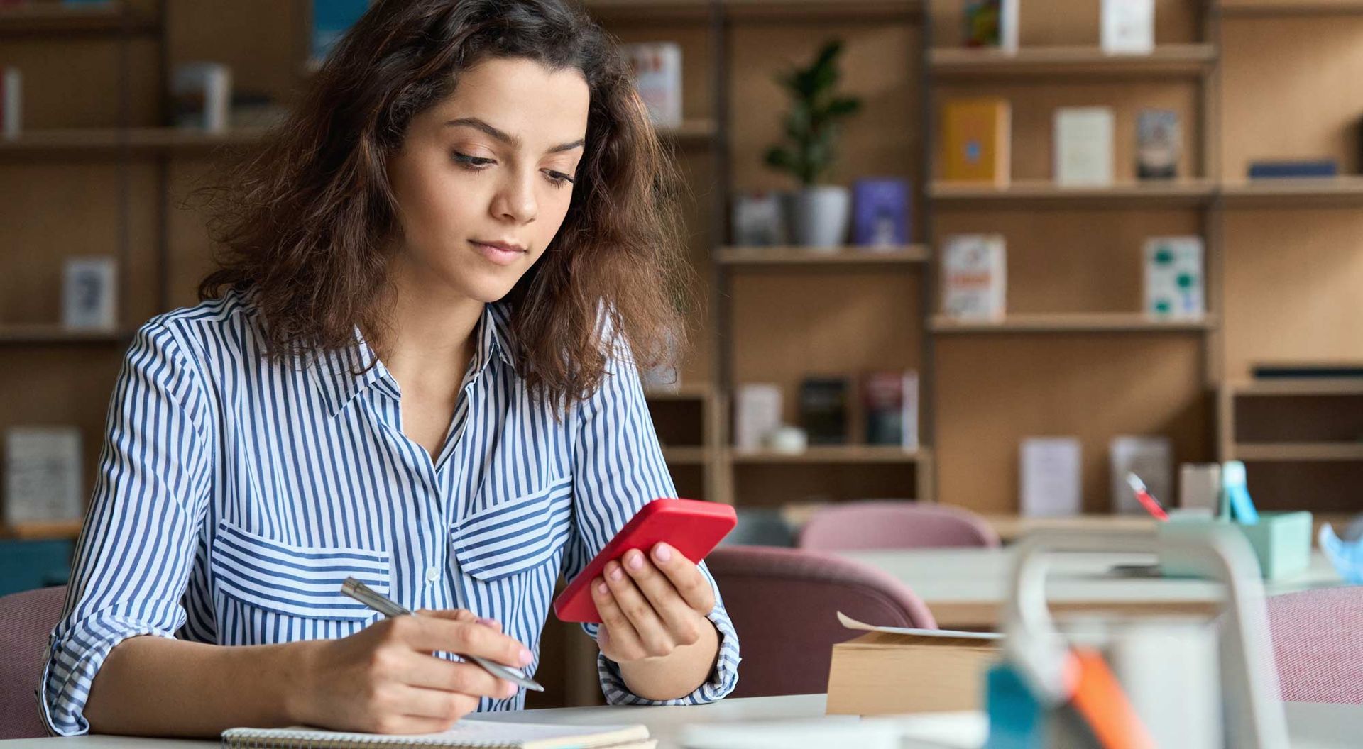 A woman is sitting at a desk looking at her college fairs app.