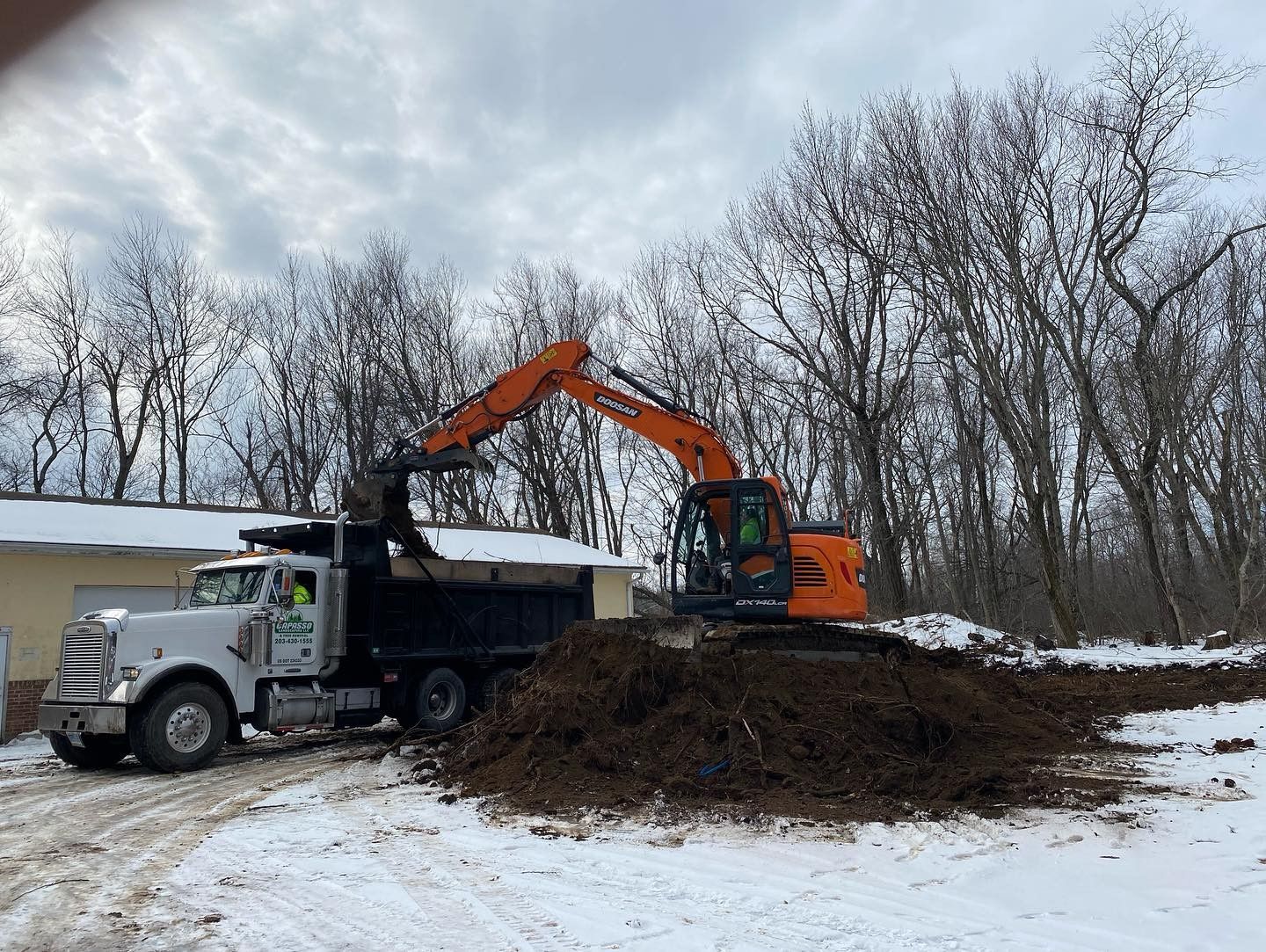 An excavator is loading dirt into a dump truck in the snow.