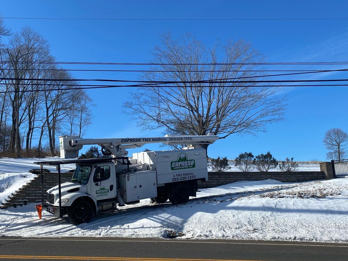 A white truck with a crane on top of it is parked on the side of the road.