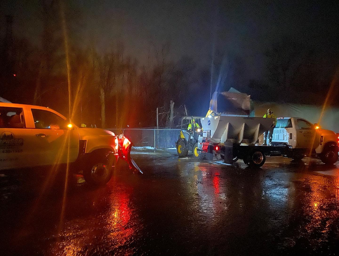Several trucks are parked on a wet road at night
