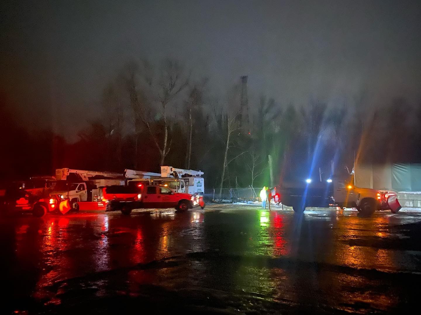 A group of snow trucks are parked in a parking lot at night.