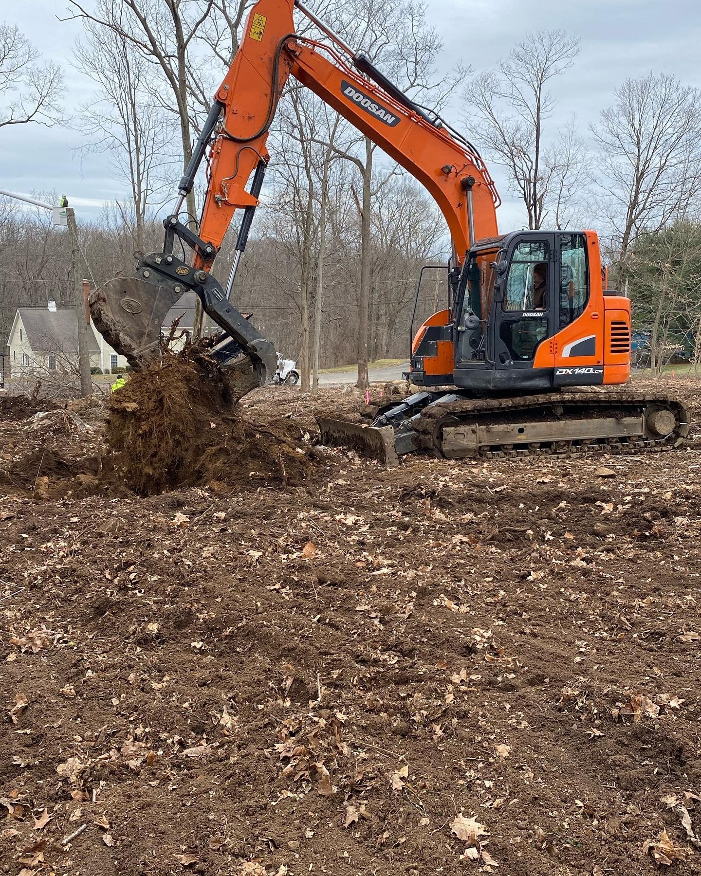 A large orange excavator is digging up a tree stump and roots.