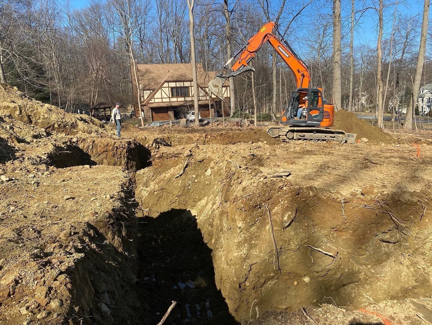 A large excavator is digging a hole in the dirt in front of a house.
