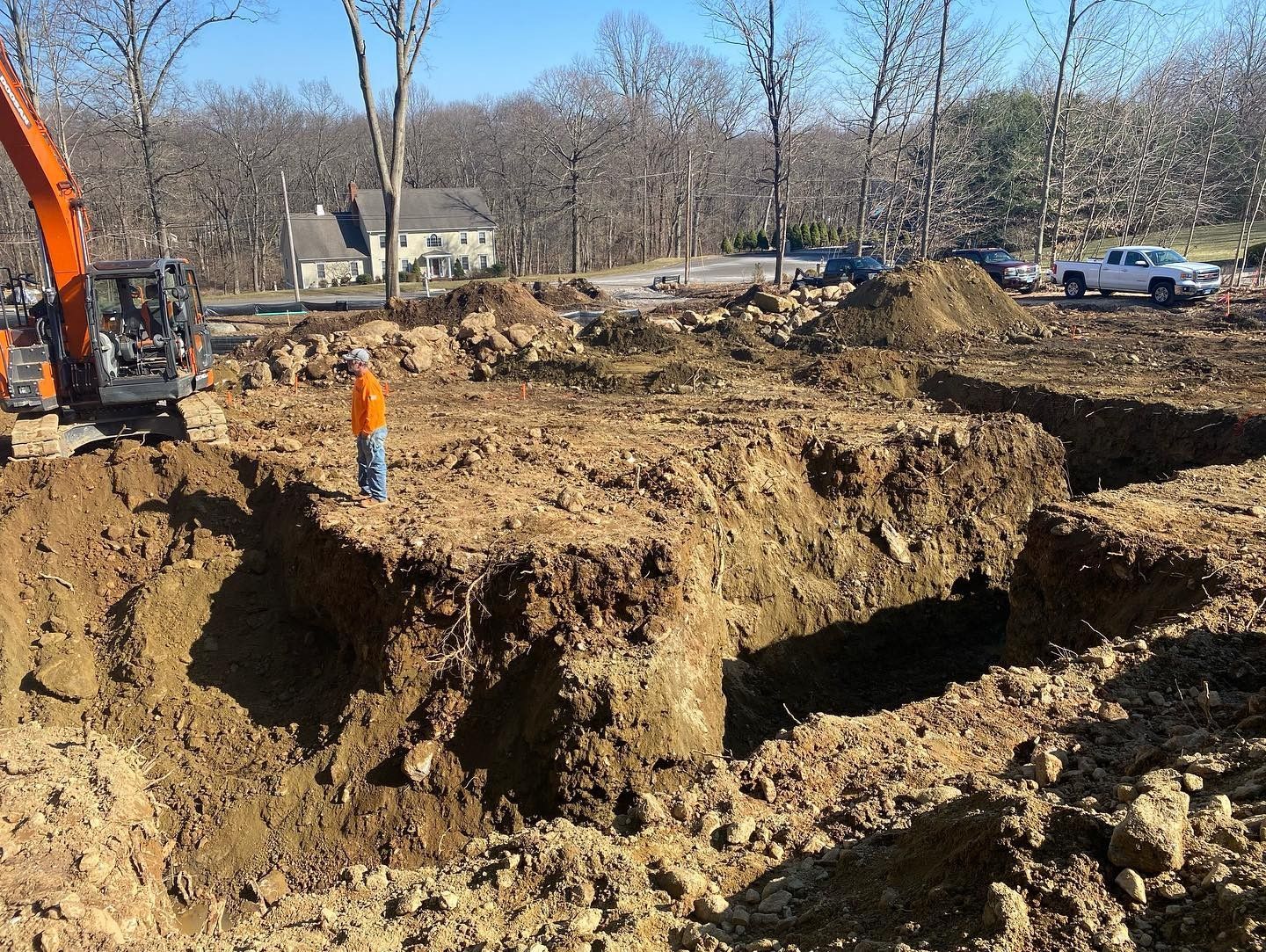 A man is standing in a pile of dirt next to a large excavator.