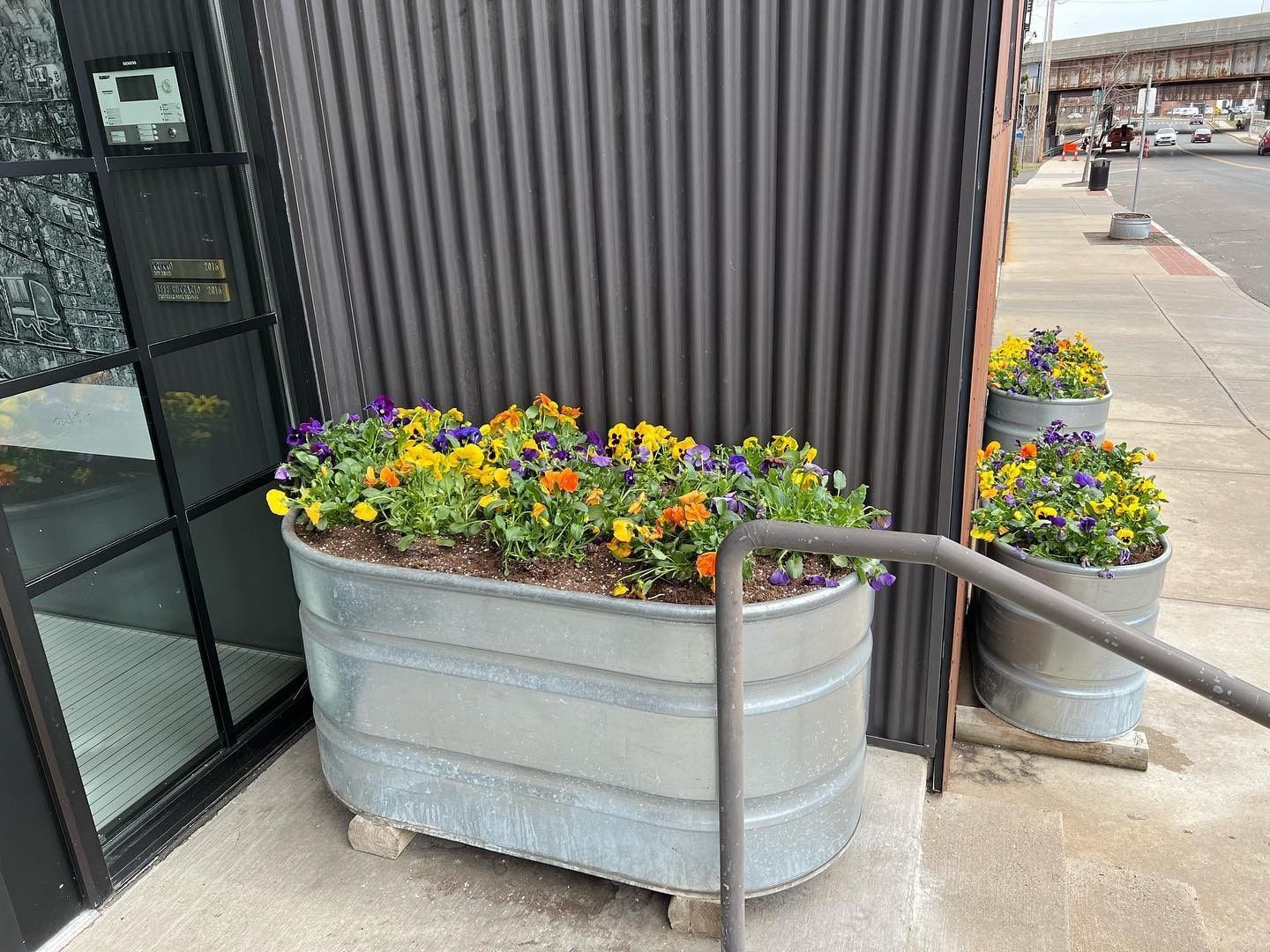 A lawn mower is cutting a lush green lawn next to a stone wall.