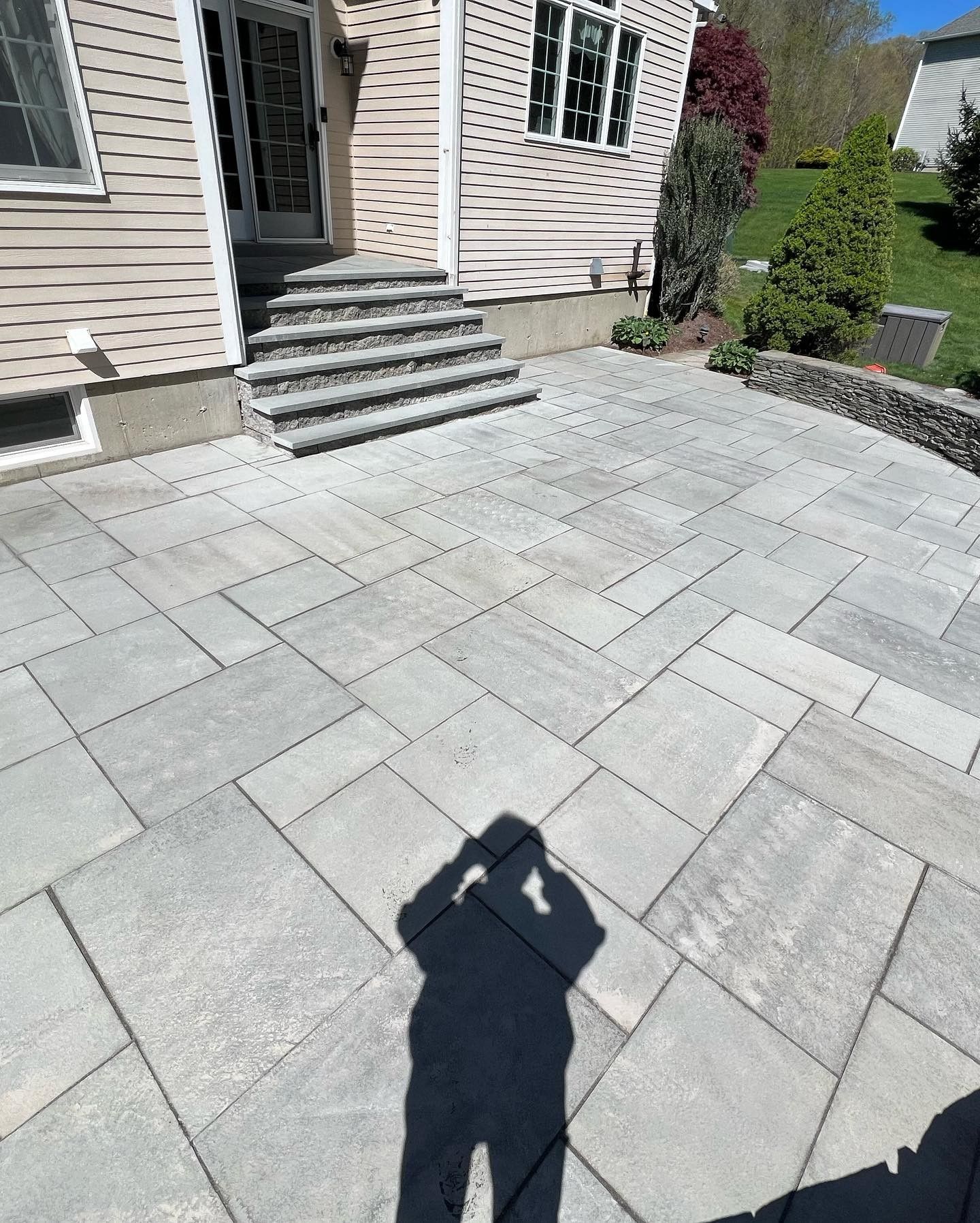 A shadow of a person is cast on a patio in front of a house.