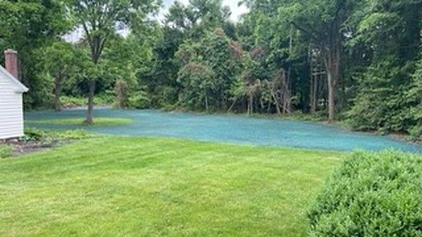 A lush green lawn with a white house in the background and trees in the background.