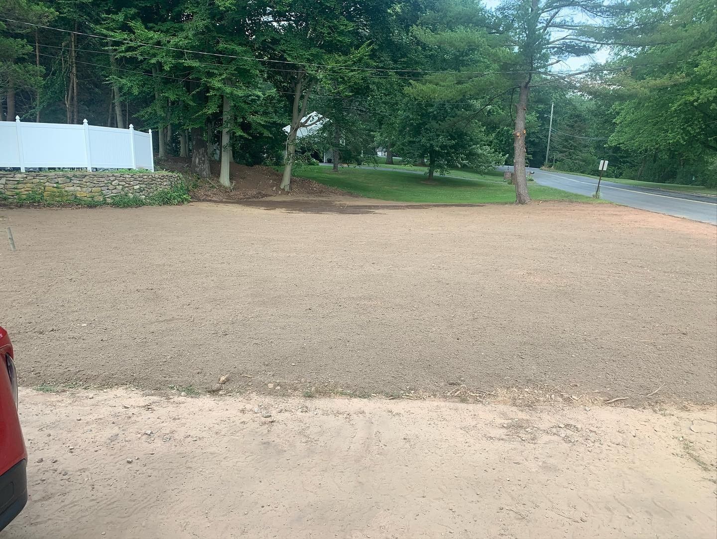 A red truck is parked in a gravel lot next to a road.