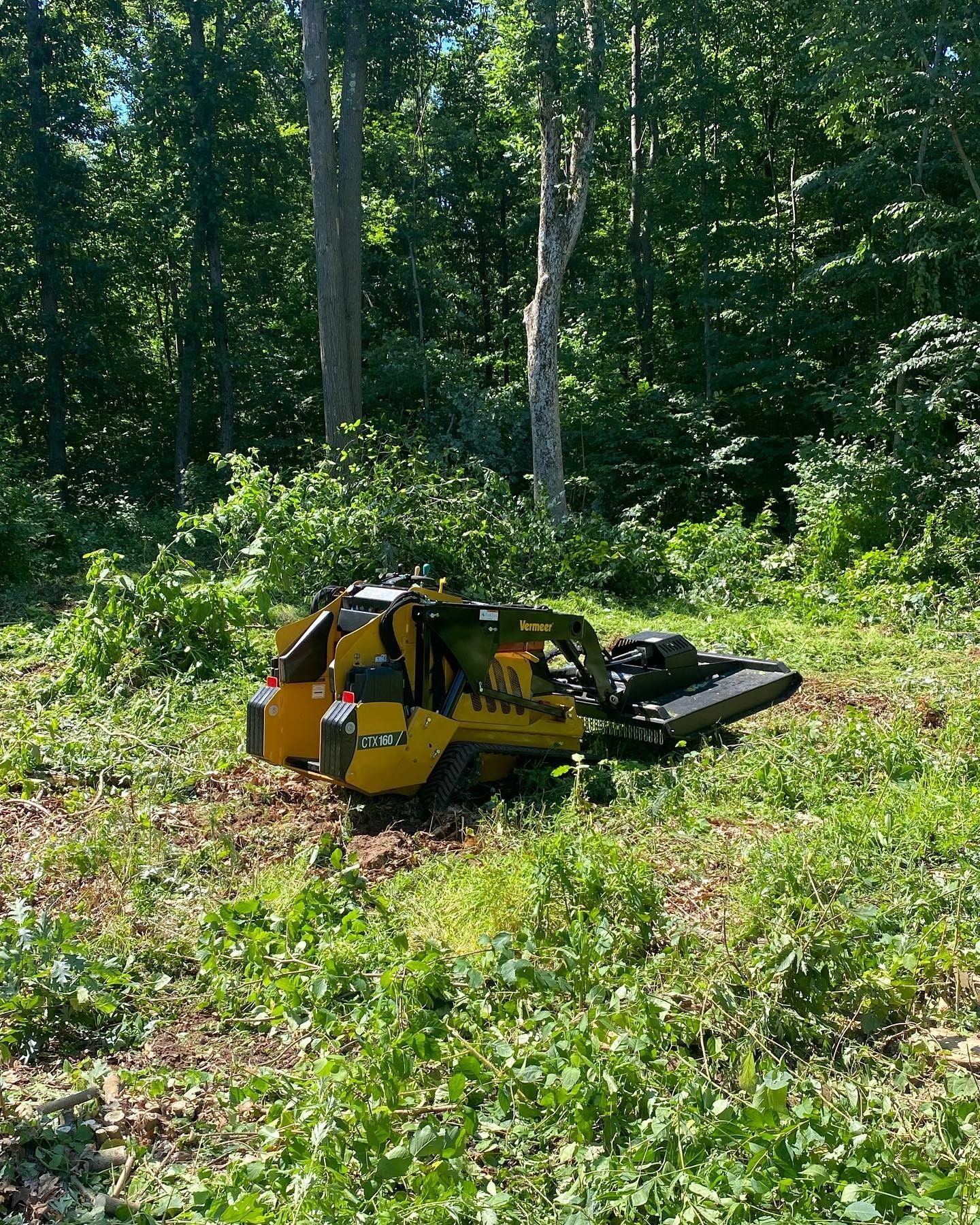 A yellow stump grinder is sitting in the middle of a grassy field.