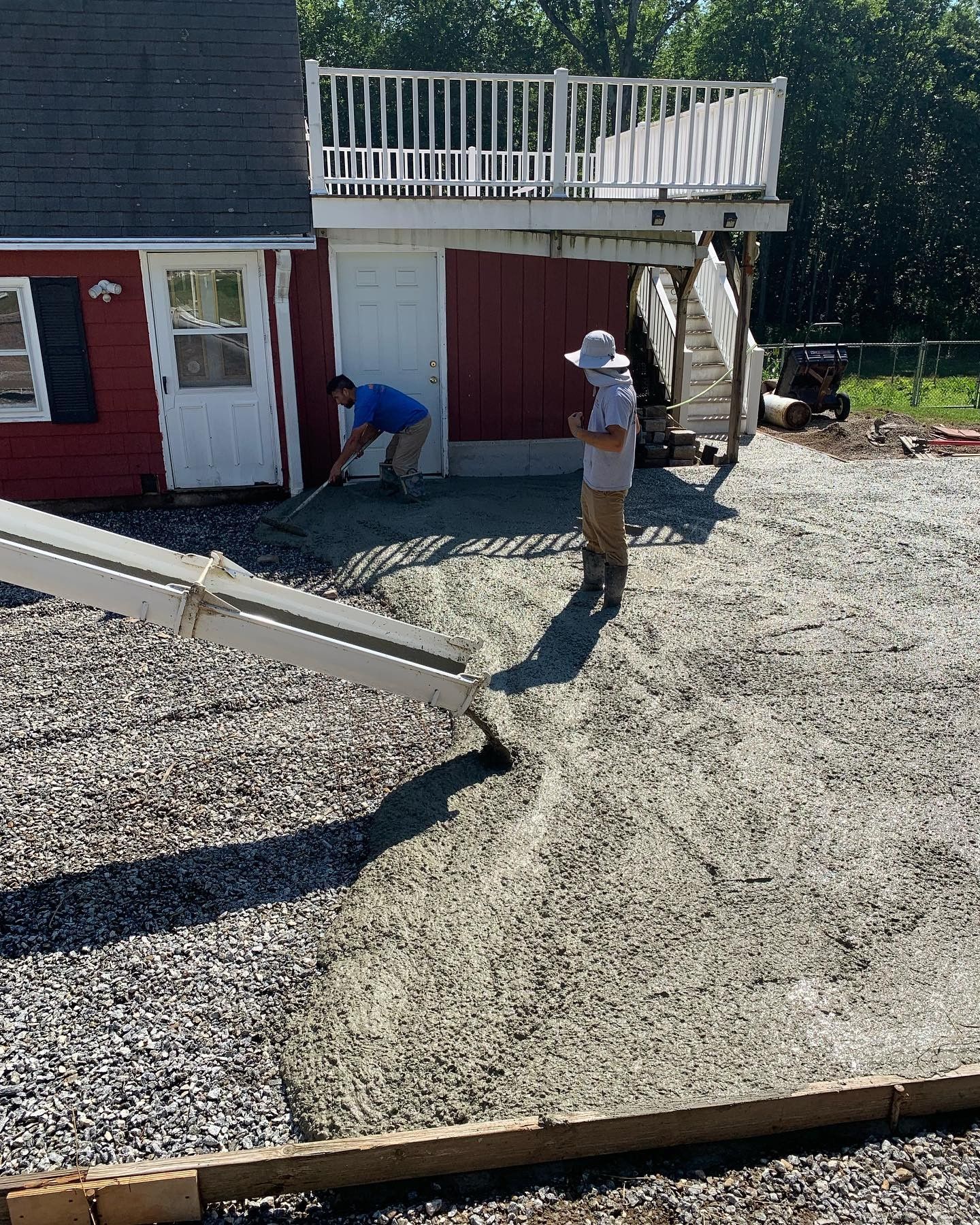 Two men are working on a driveway in front of a red house.