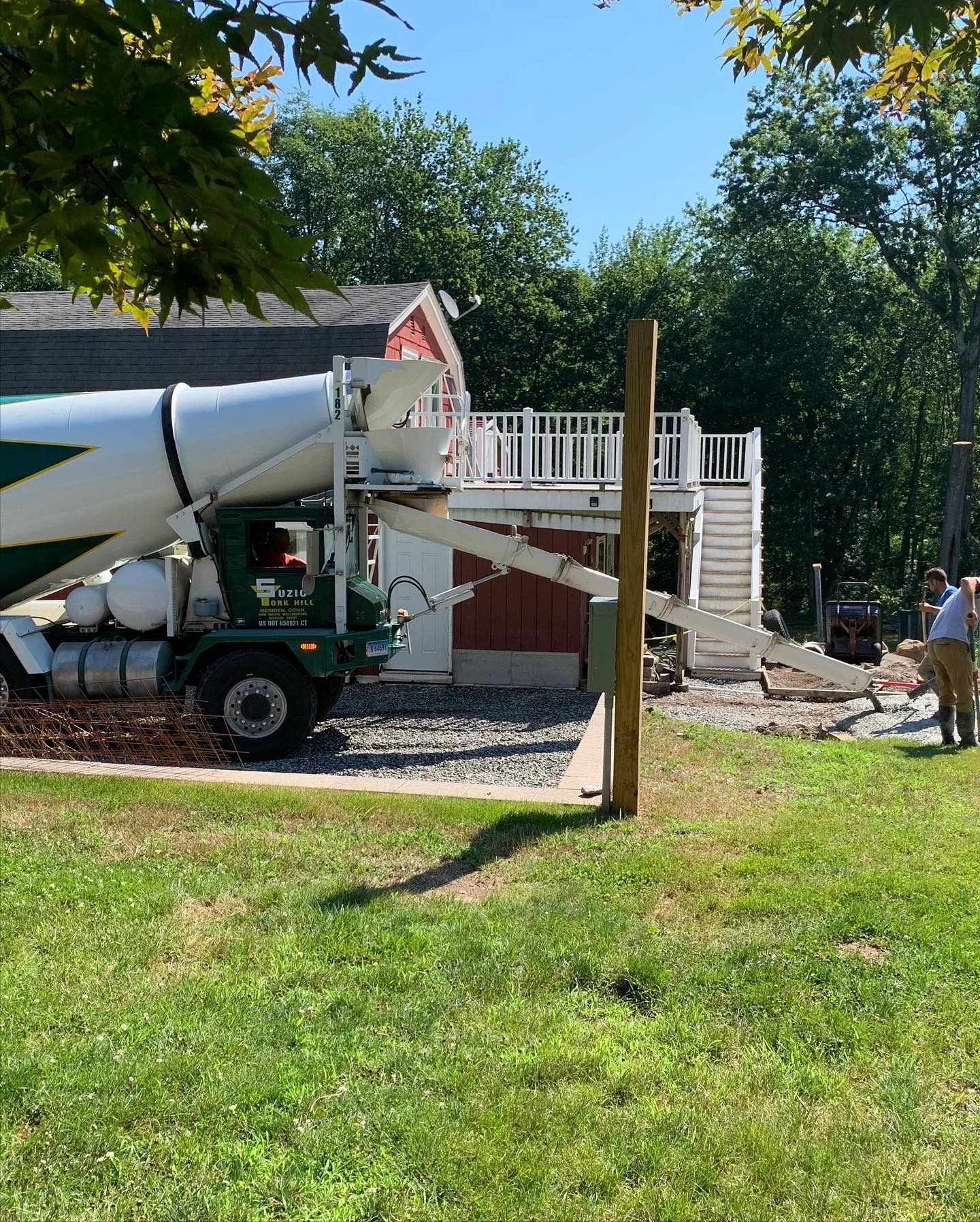 A concrete truck is pouring concrete into a driveway in front of a house.