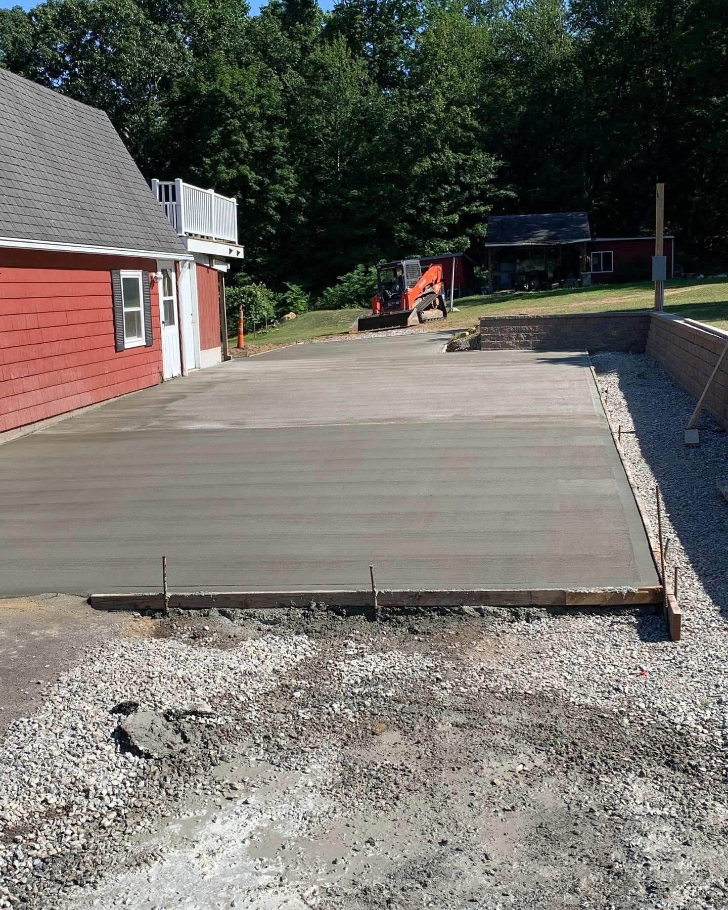 A concrete driveway is being built in front of a red house
