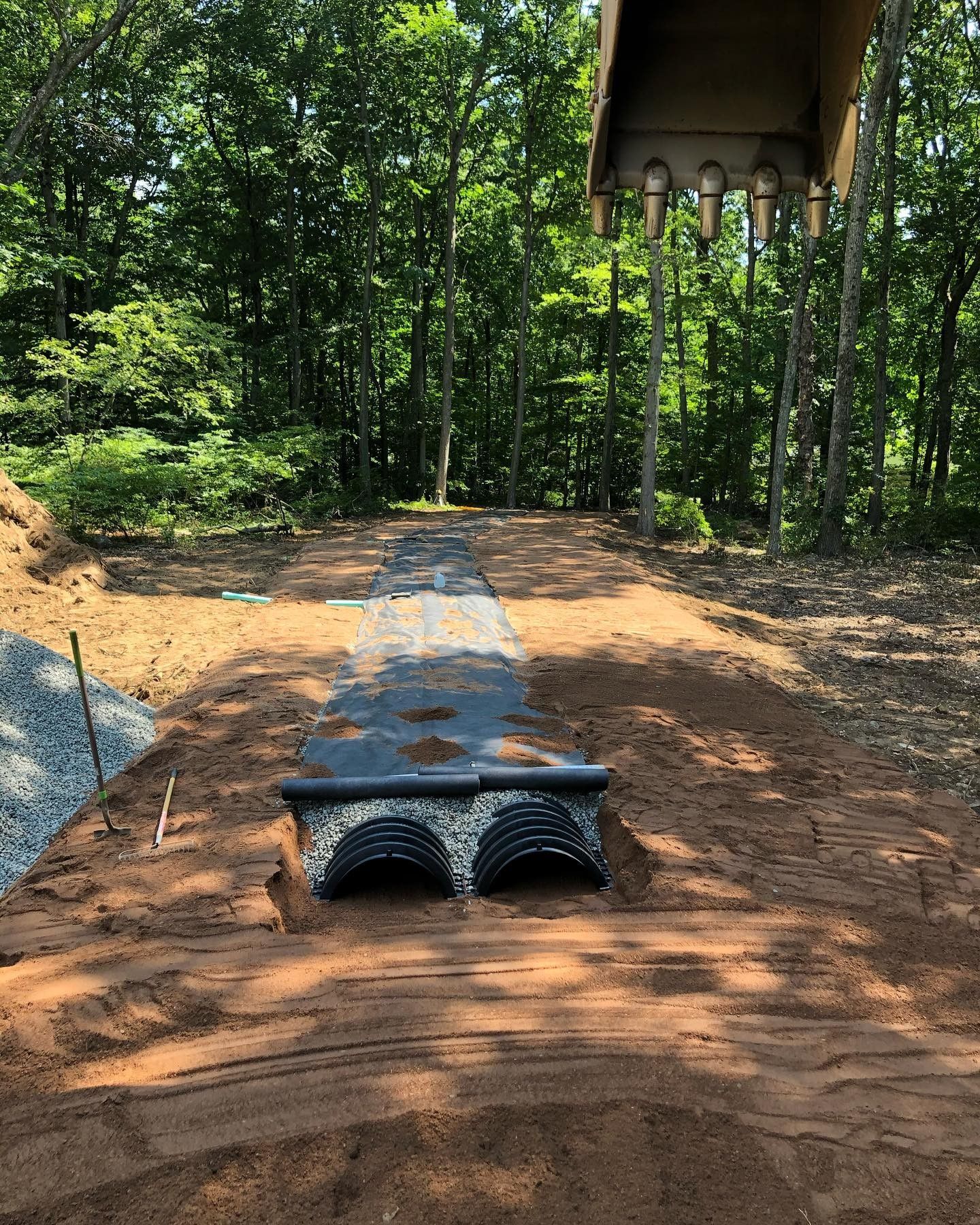 A large excavator is digging a hole in the dirt in the middle of a forest.