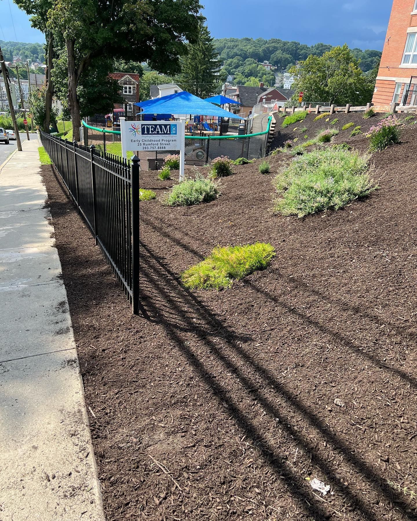 Three metal planters filled with flowers are sitting on a sidewalk in front of a brick building.