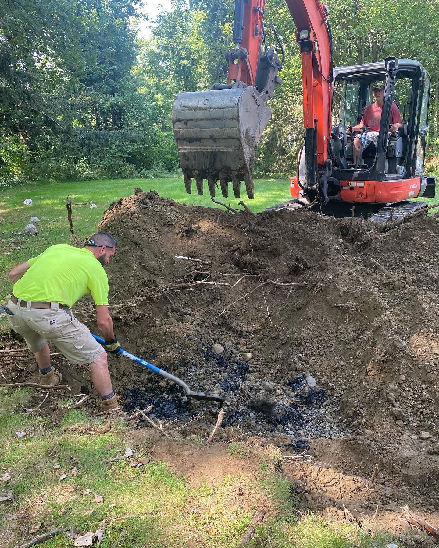 A man is digging in the dirt next to an excavator.