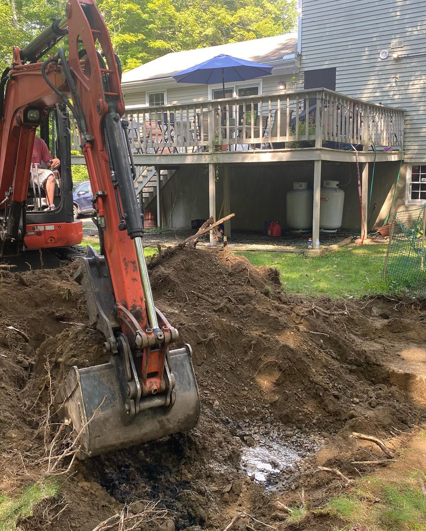 An excavator is digging a hole in the dirt in front of a house.