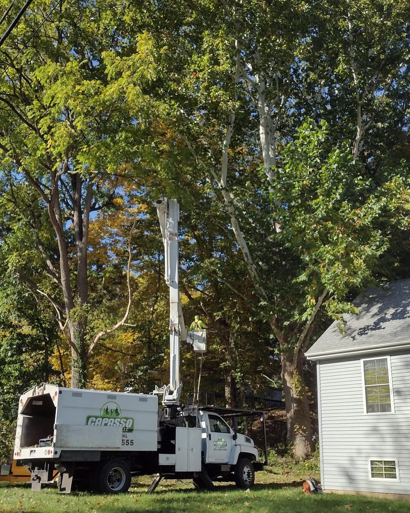 A white truck with a crane attached to it is parked in front of a house.